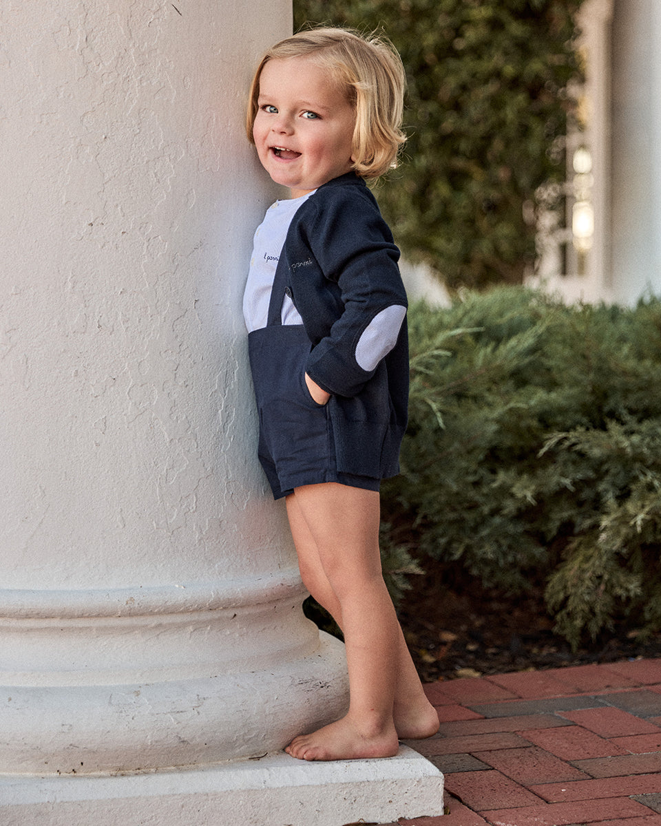 Child in a navy outfit standing on a stone step outdoors
