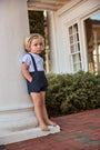 Child in a white shirt and navy shorts standing on a stone step outdoors.