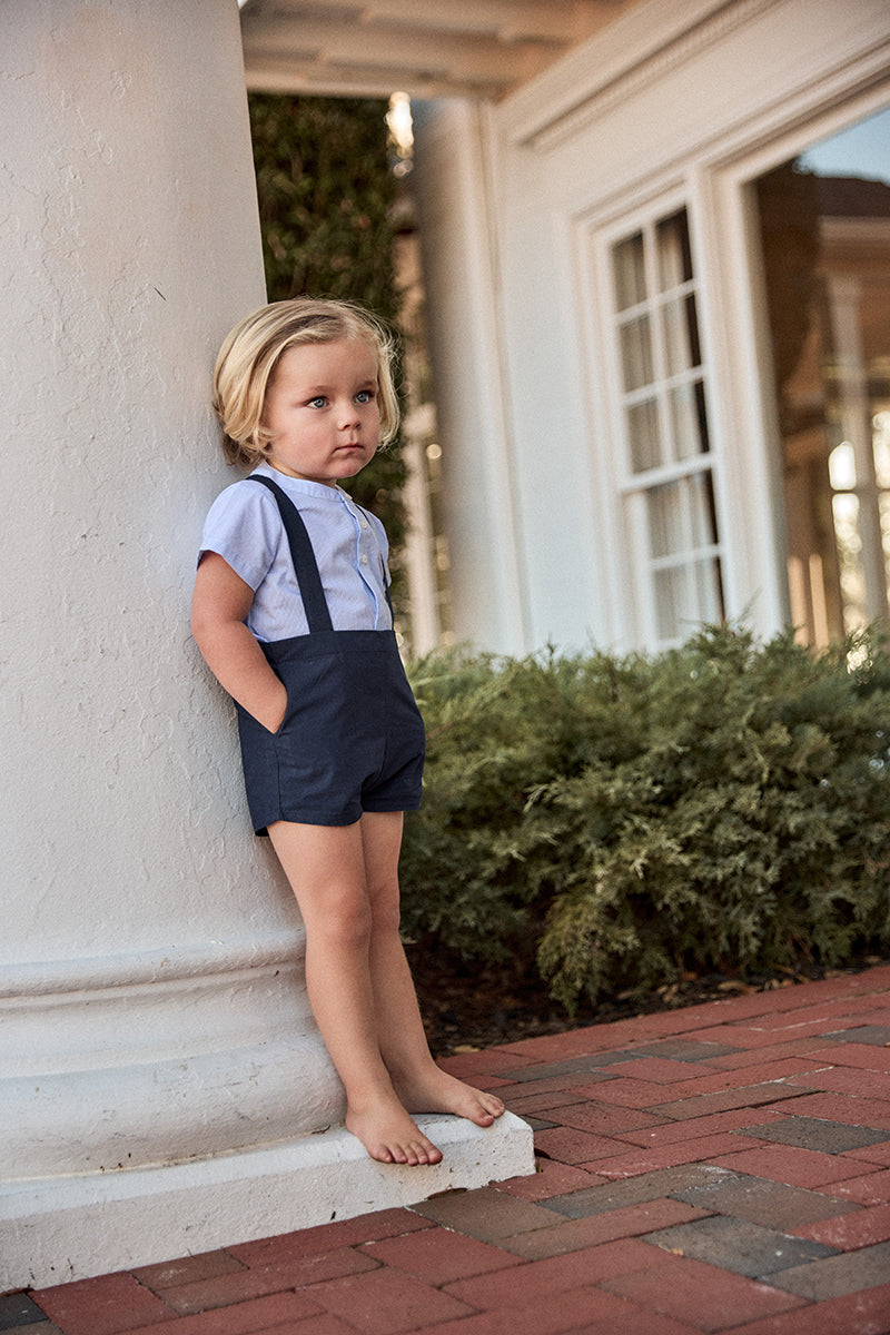 Child in a white shirt and navy shorts standing on a stone step outdoors.