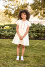 Young girl in a white dress standing on grass with trees in the background