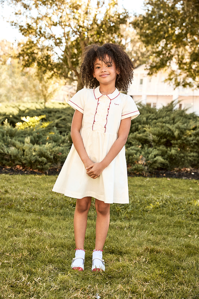 Young girl in a white dress standing on grass with trees in the background