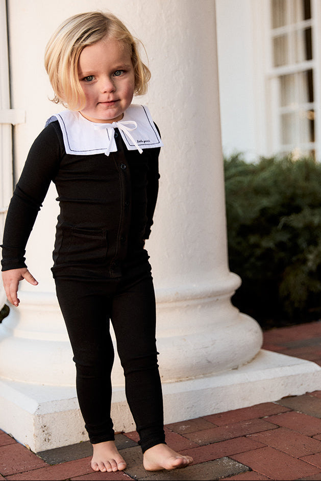 Child in a black outfit with white collar standing on a brick path.