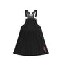 A black denim overall dress for kids, featuring adjustable shoulder straps with silver metal buttons, a front patch pocket, and a small embroidered character on the lower left hem.