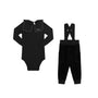 A two-piece baby clothing set in black velvet, featuring a long-sleeve bodysuit with a structured collar and a pair of matching pants with suspenders, displayed on a solid white background.