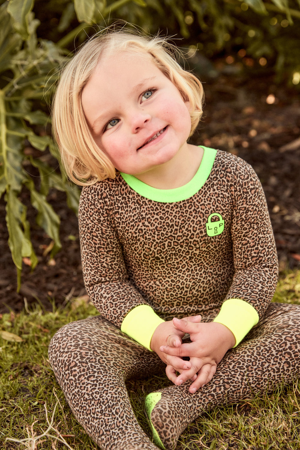 Child wearing a leopard print outfit with green accents sitting outdoors.