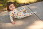 Child wearing a colorful onesie with letter patterns on a concrete surface.