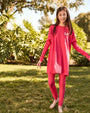Teen wearing a pink outfit with 'L.P.' on it, standing in a grassy area with trees.