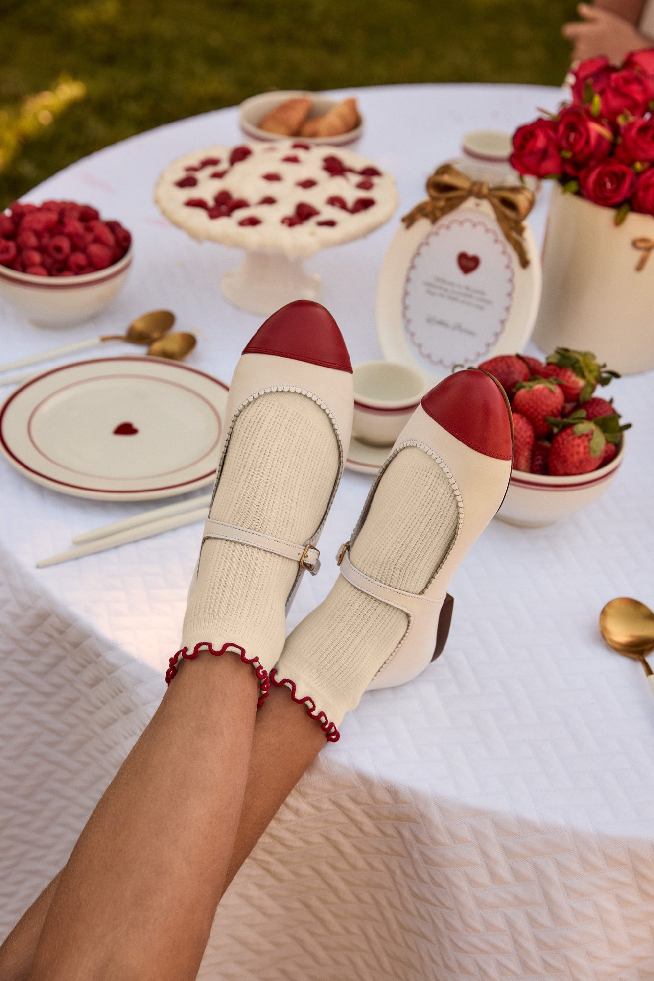 Pair of beige shoes with red soles on a picnic table with strawberries and other food.