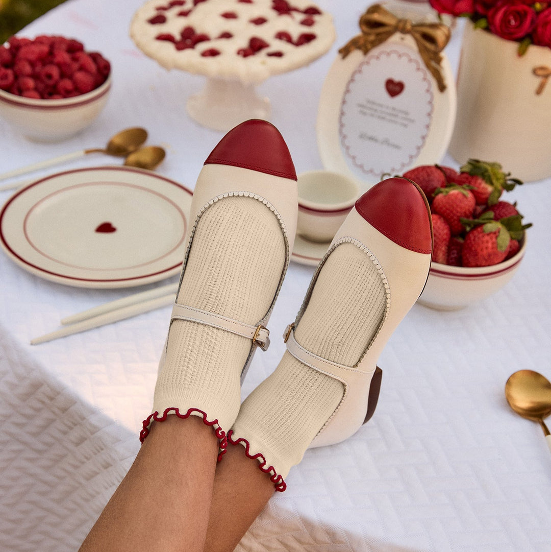 Pair of beige shoes with red soles on a picnic table with strawberries and other food.