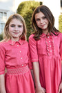 Two young girls wearing matching pink dresses outdoors.