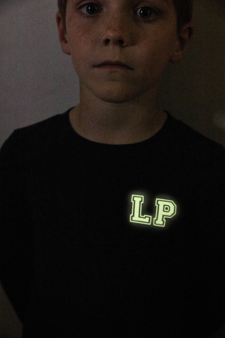 Child wearing a black shirt with 'LP' on it in a dark setting