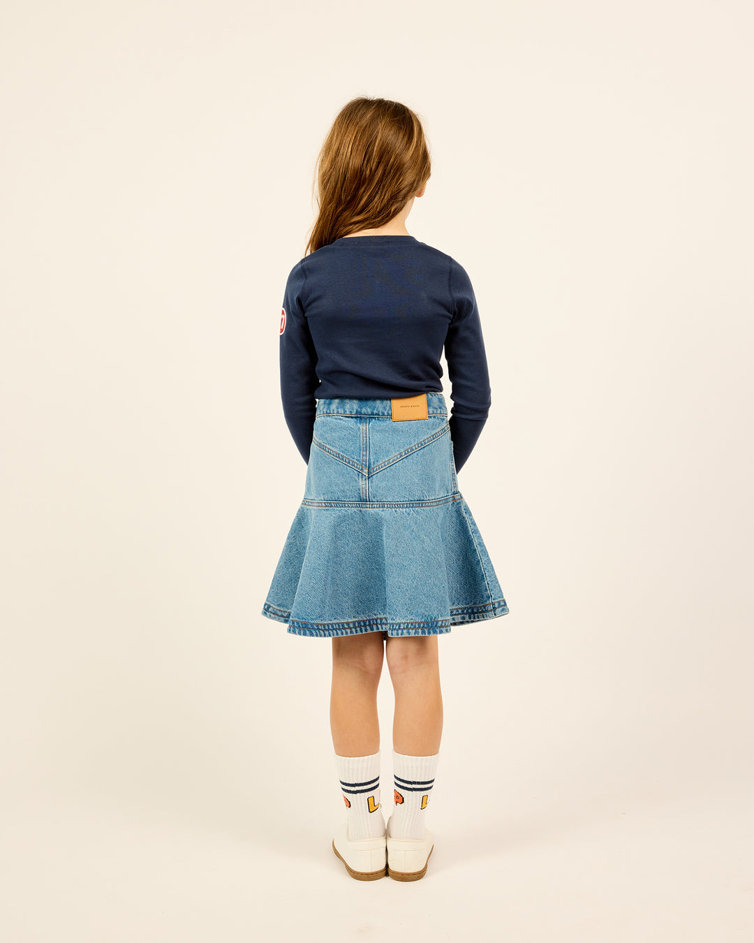 The backside of the model wearing the Short Ruffle Denim Skirt in Blue.