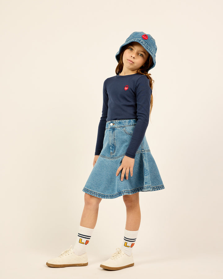 Model wearing the Short Ruffle Denim Skirt in Blue and the blue Long Sleeve Heart Logo Tee.