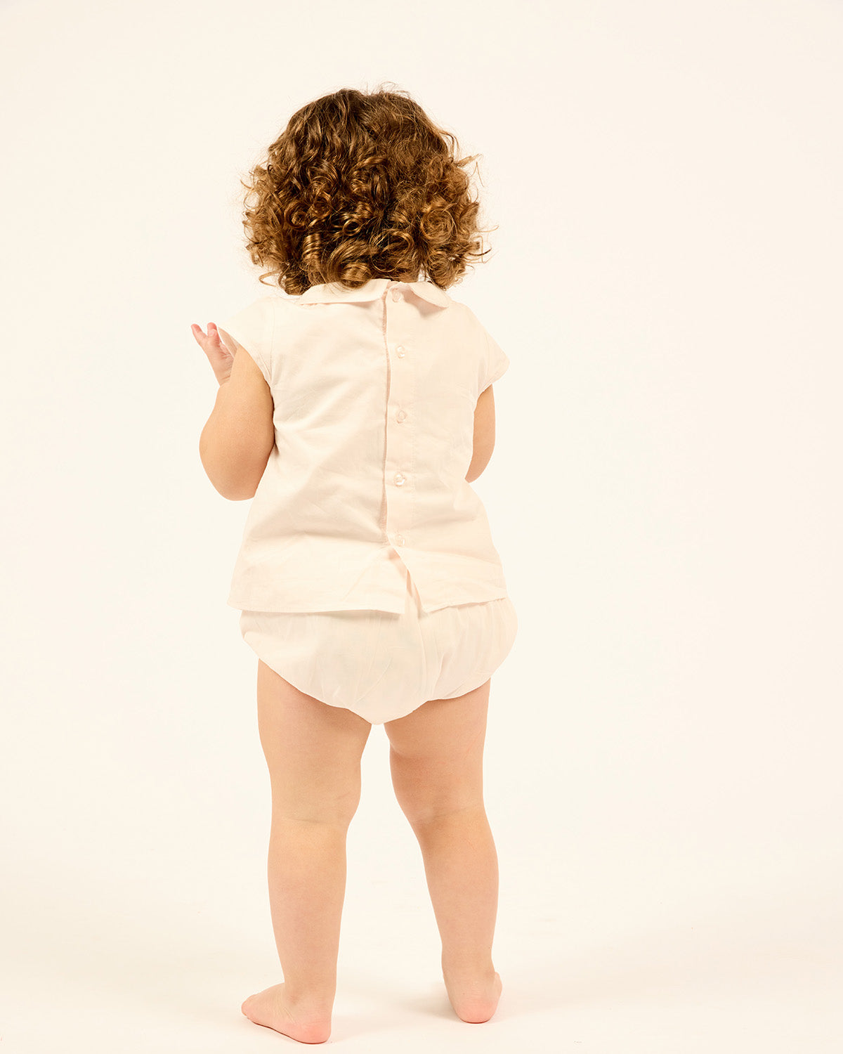 Baby wearing the Two-piece Cotton Set With Bloomers in White, back view.