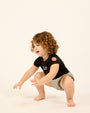 Baby wearing LP Est. 17 Baby Bodysuit in Black with denim bloomers.