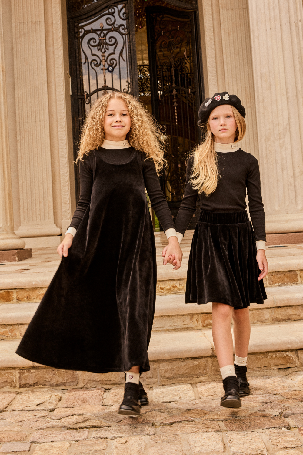 Two young girls in black dresses standing on stone steps with classical architecture in the background.