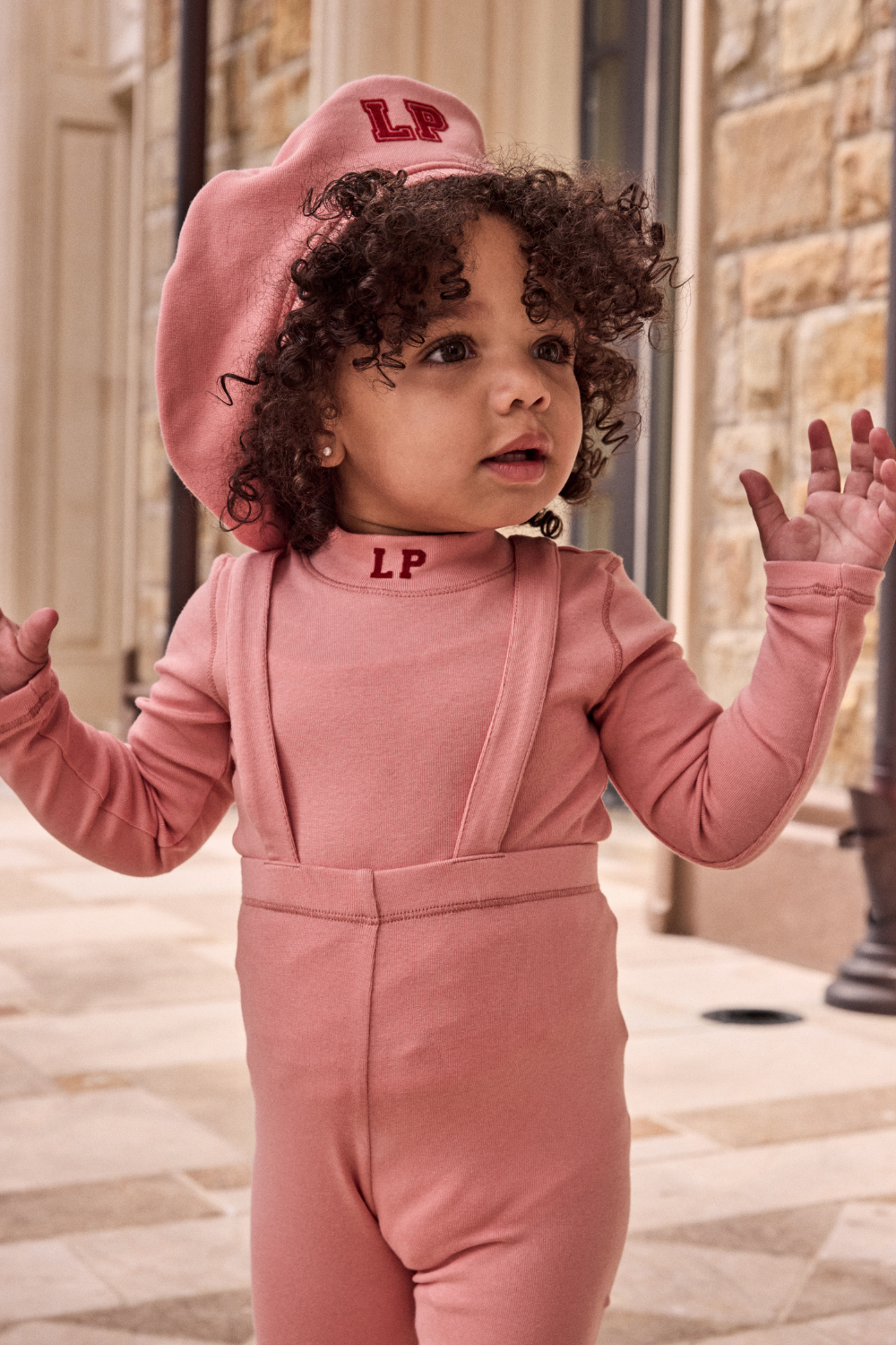 Child wearing a pink outfit with 'LP' branding, standing outdoors.