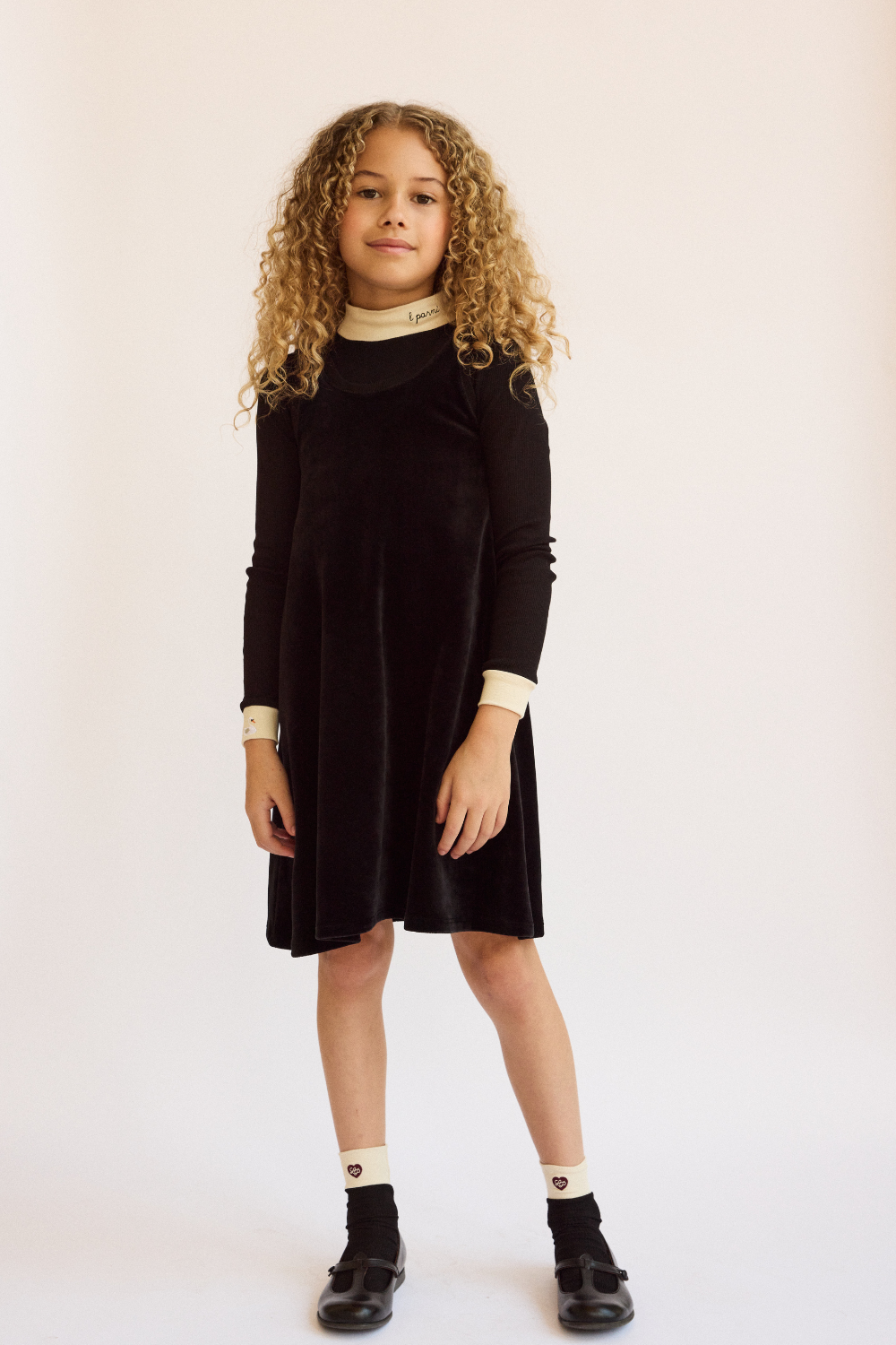 Young girl wearing a black dress with long sleeves on a plain background.