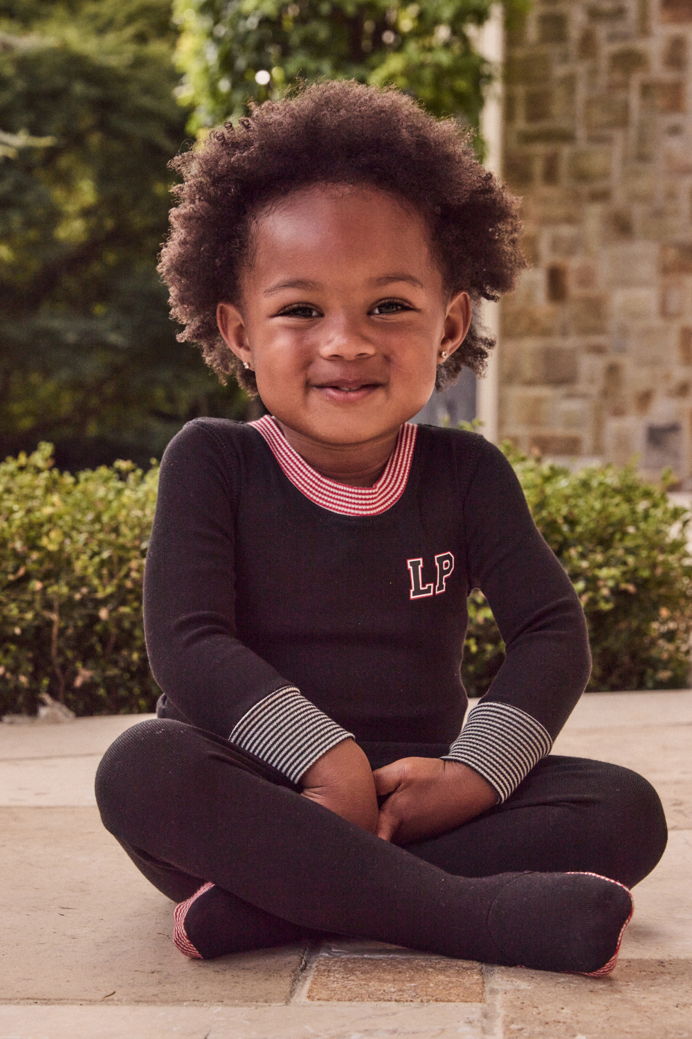 Child sitting outdoors wearing a dark outfit with a visible brand logo.