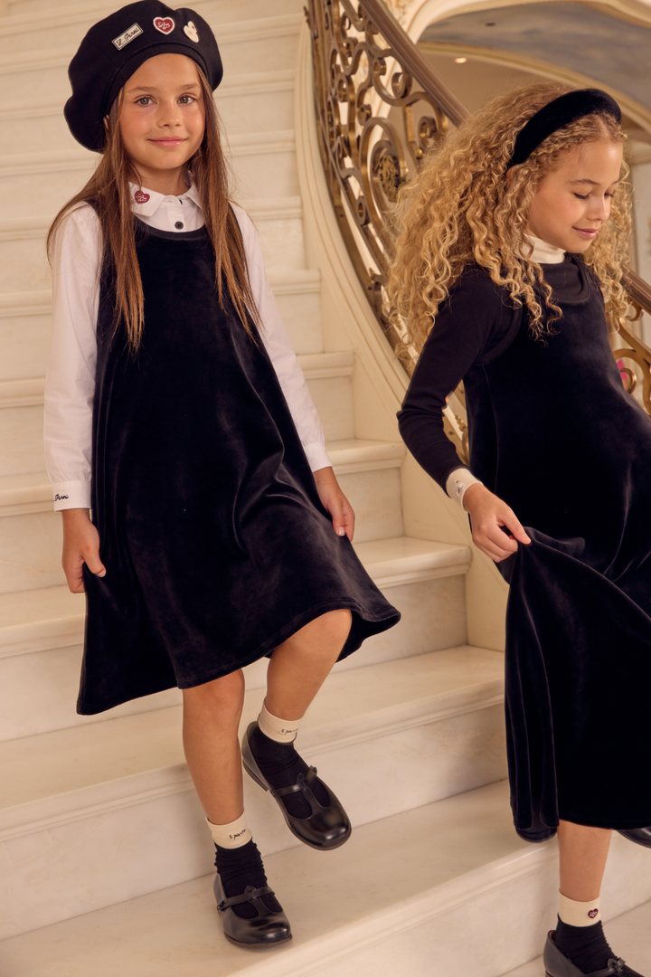 Two young girls in matching black dresses and hats standing on a staircase.