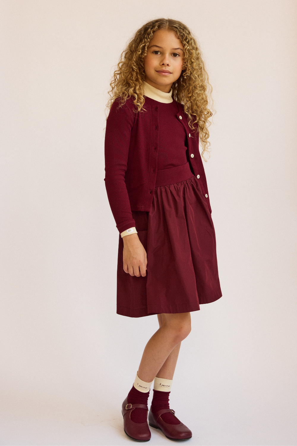 Young girl wearing a burgundy dress with a white collar against a beige background