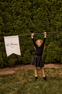 Young girl holding a banner with 'L' Parini' branding against a green hedge.
