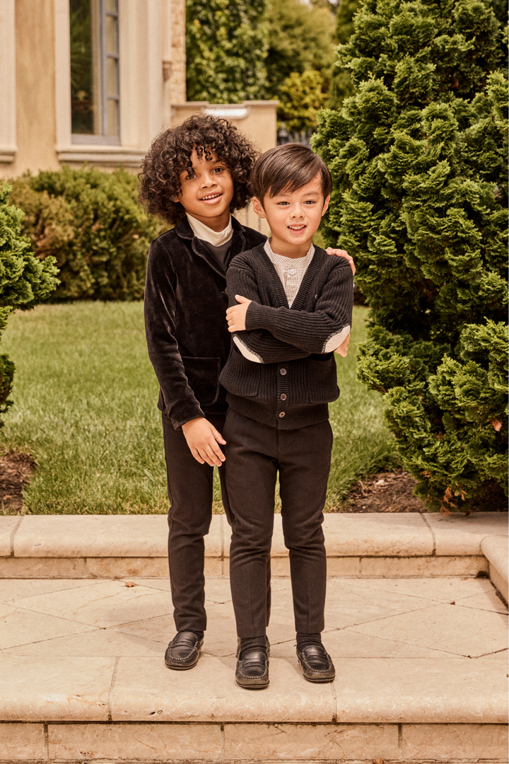 Two young boys in matching outfits standing outdoors on a stone ledge.