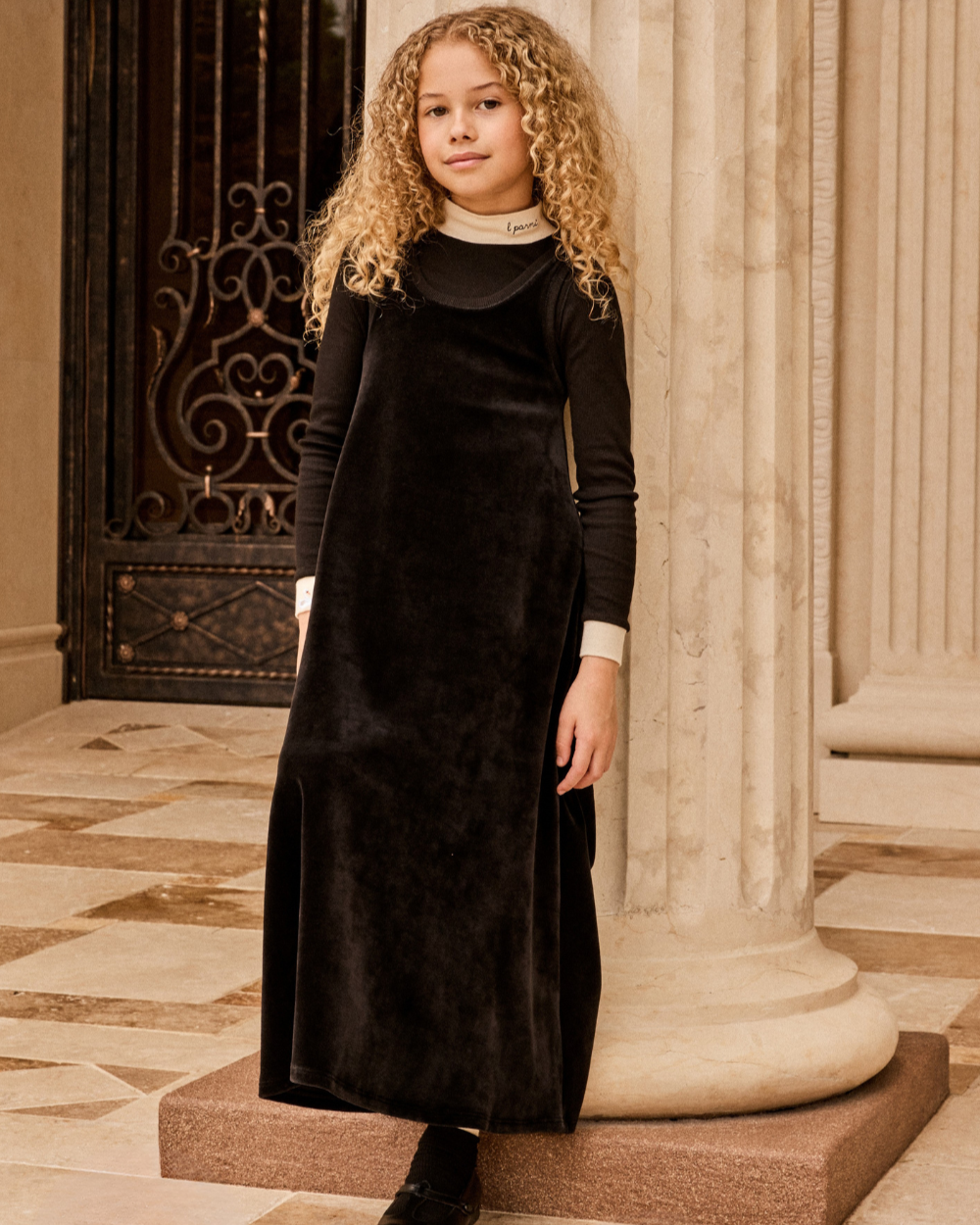 Young girl in a black dress standing in an elegant interior setting with columns.