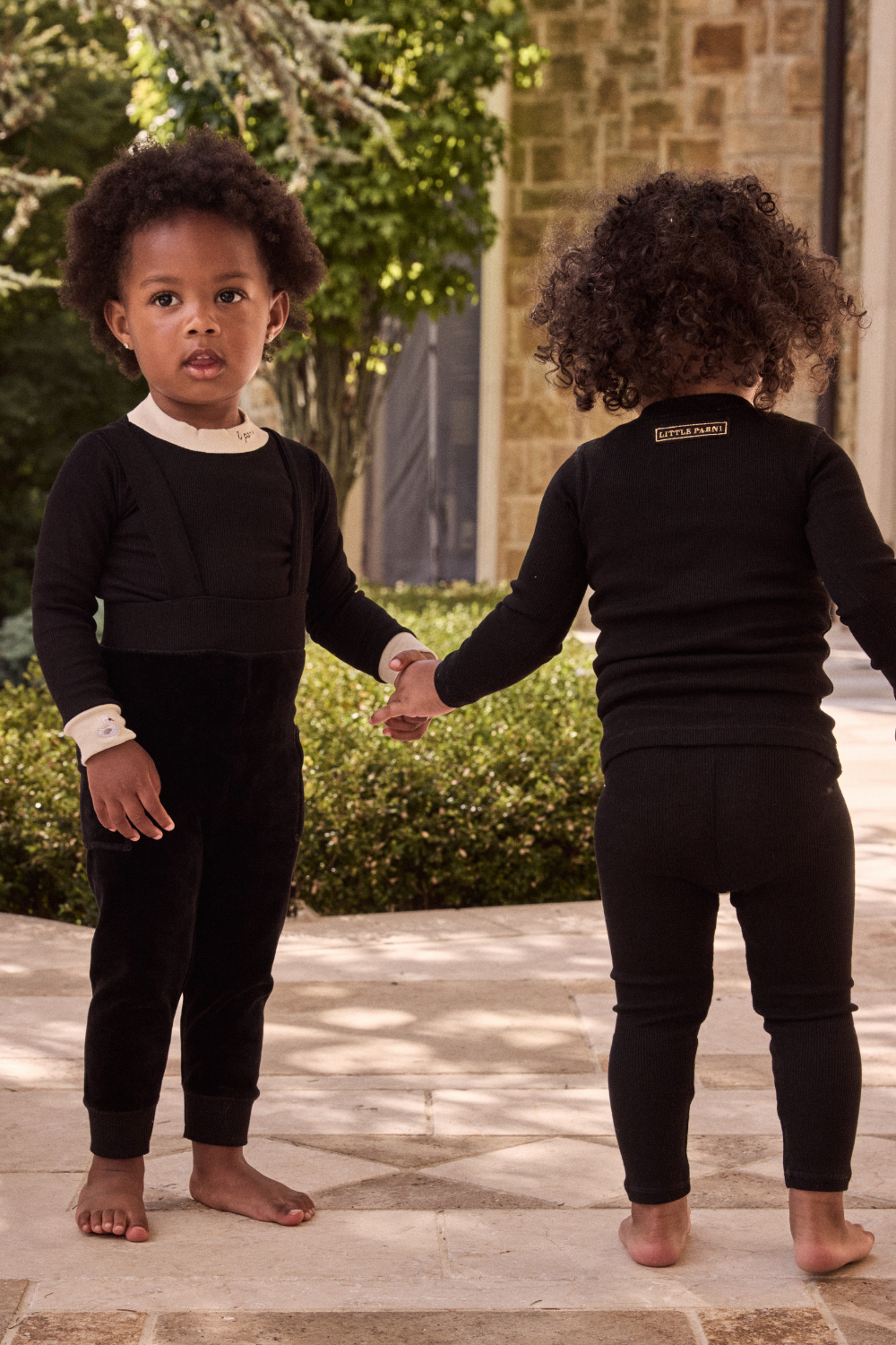 Two children in matching black outfits standing on a stone patio.