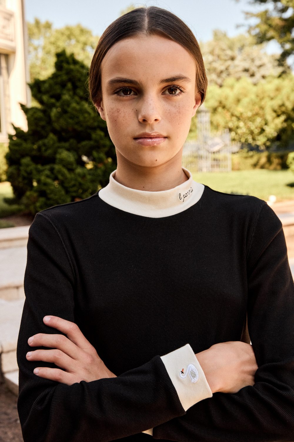 Person wearing a black outfit with a white collar in an outdoor setting.