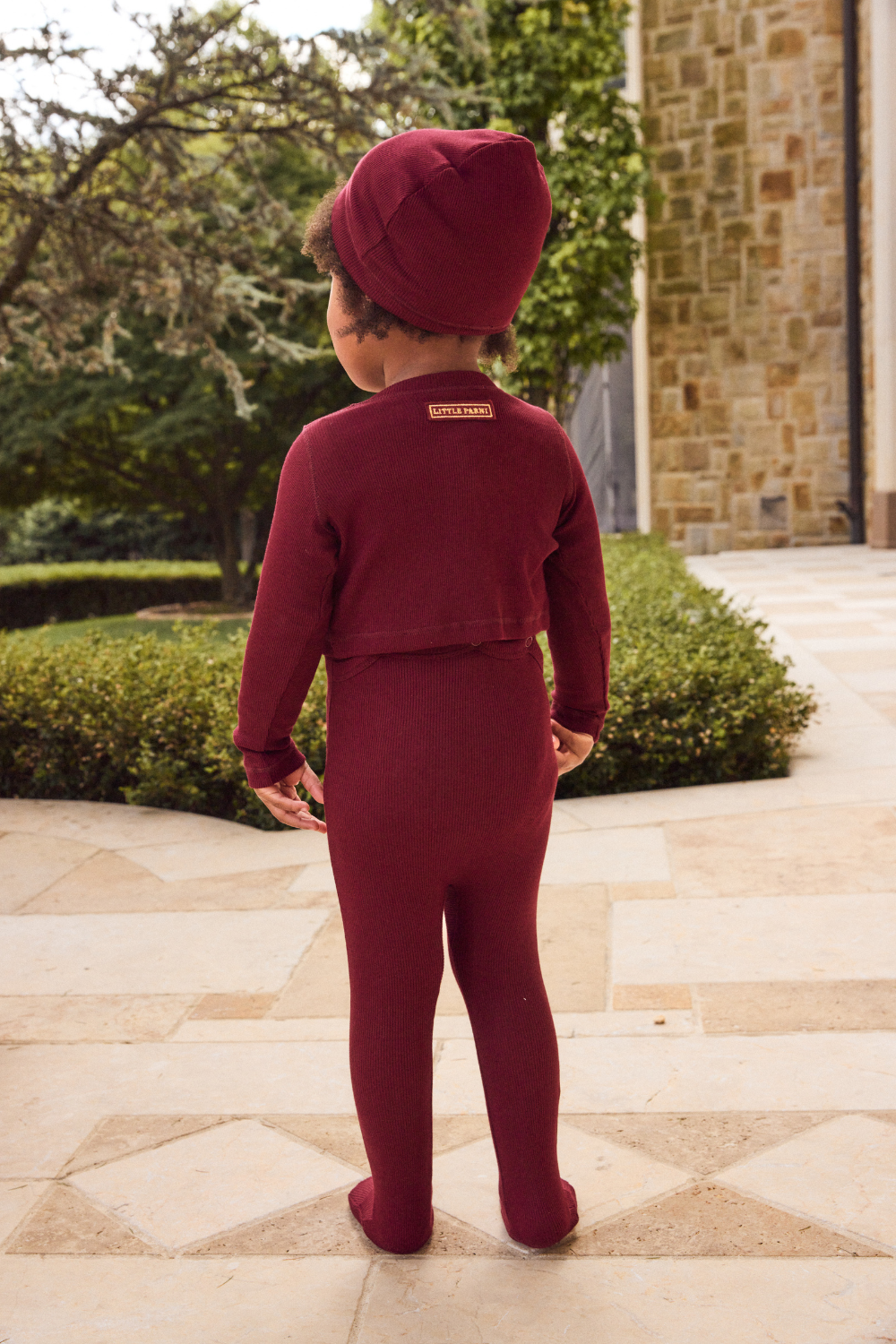 Child wearing a maroon outfit with a matching hat standing on a stone path.