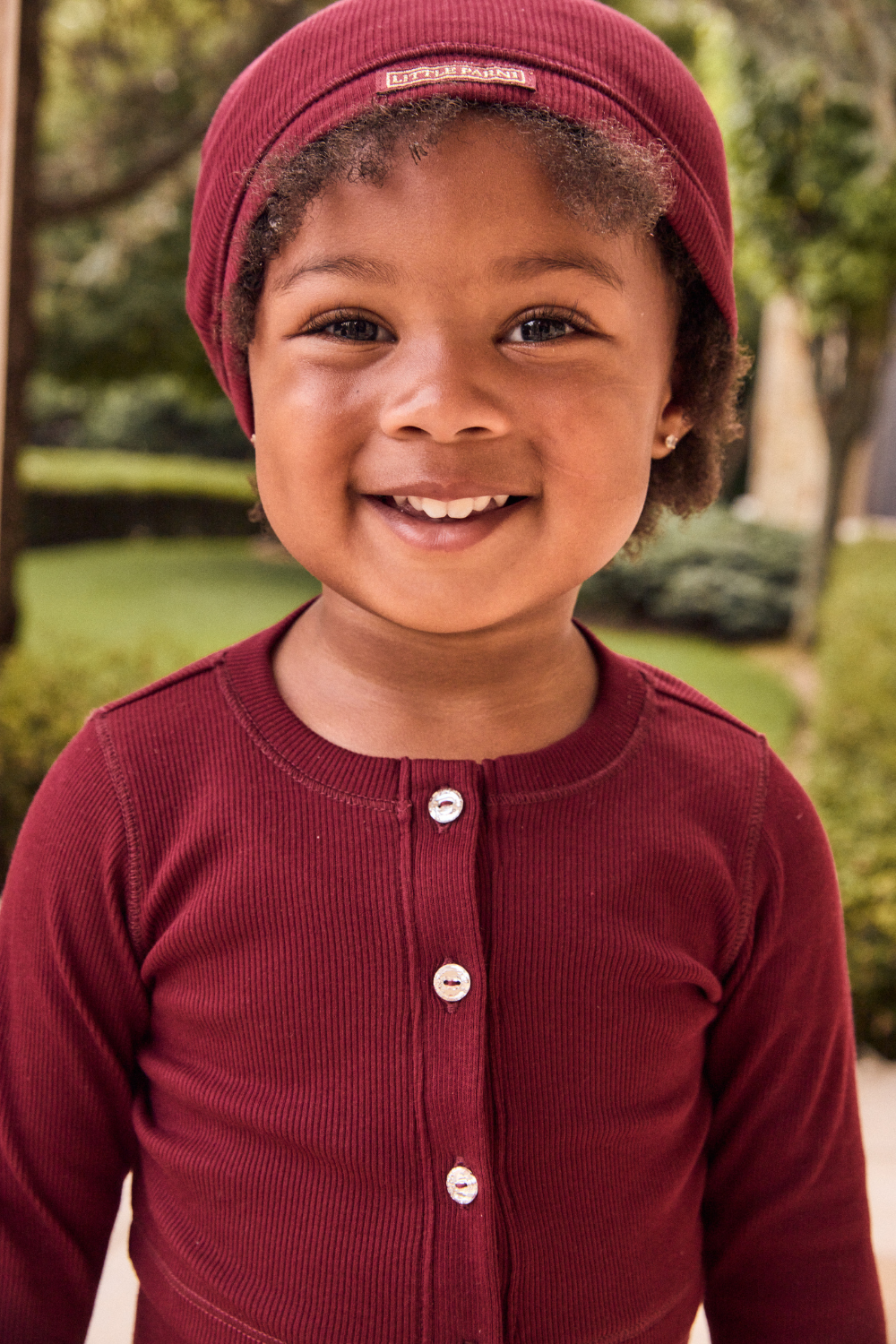 Child wearing a maroon outfit with a matching hat outdoors.
