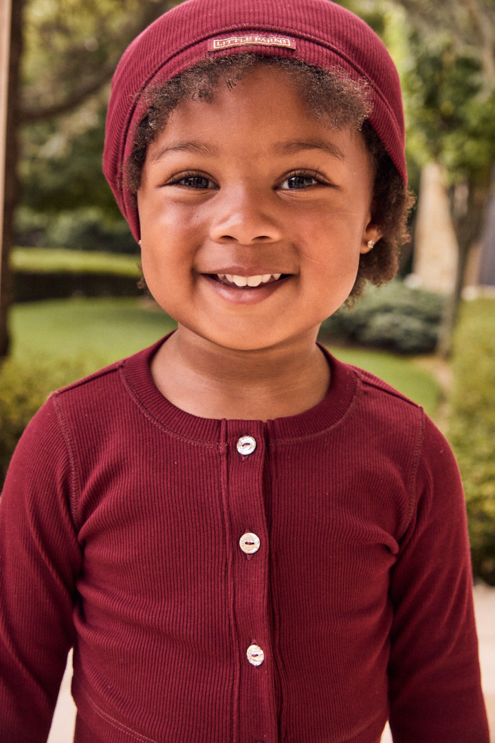 Child wearing a maroon outfit with a matching hat outdoors.