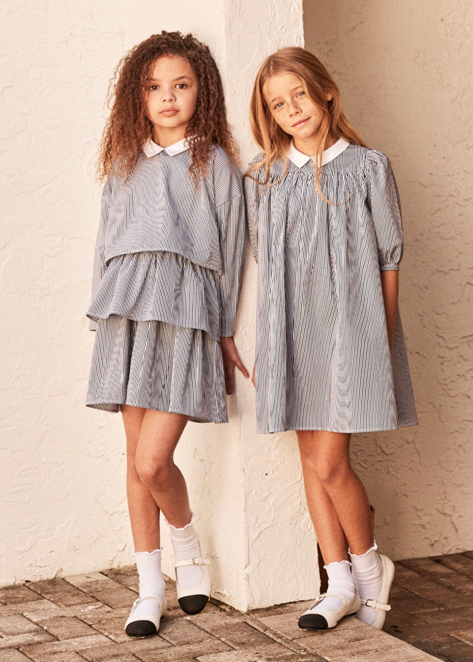 Two girls standing together outside, one wearing the ruffle skirt and matching cropped top and one wearing an empire waist dress in black and white stripe
