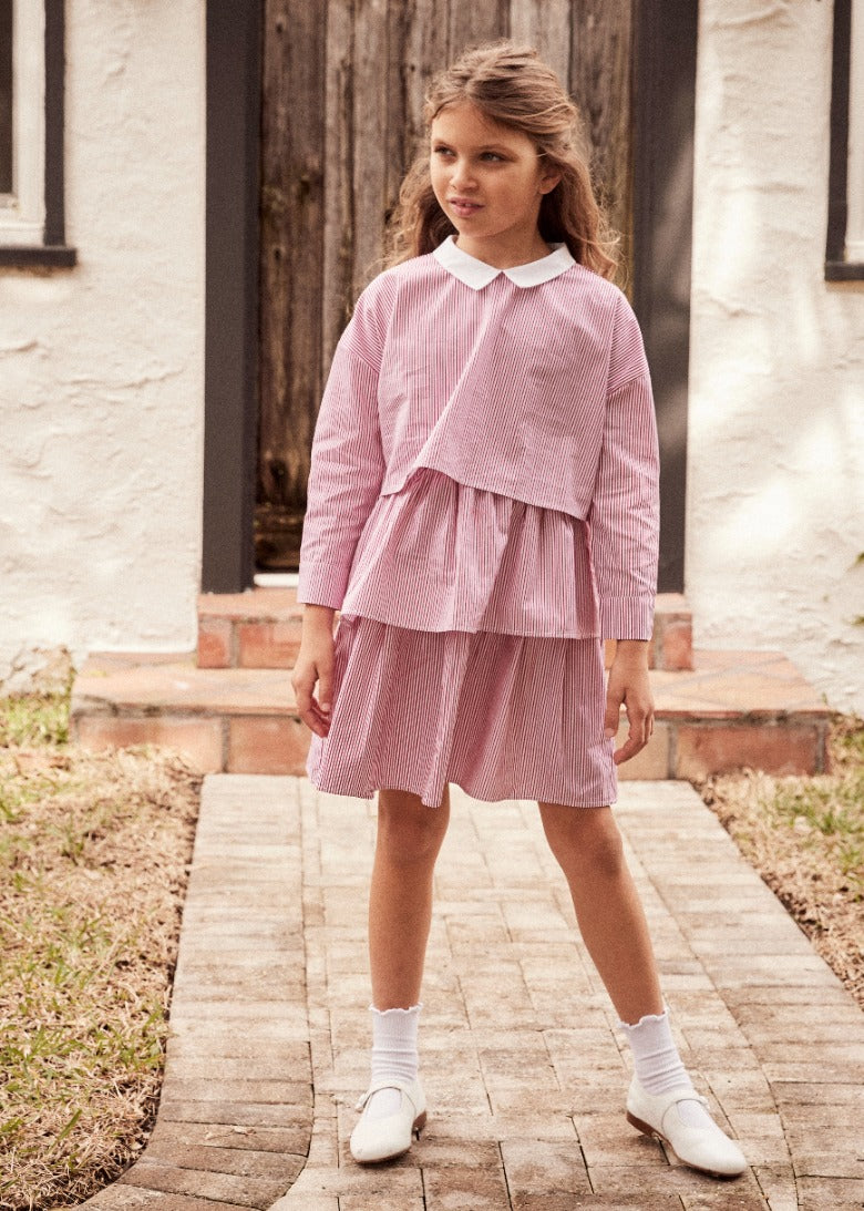 Little girl standing on a walkway outside wearing a pink and white striped cropped top and matching ruffle skirt
