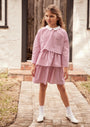 Young girl wearing a cropped long sleeve top with a peter pan collar and matching tier skirt standing outside on a walkway