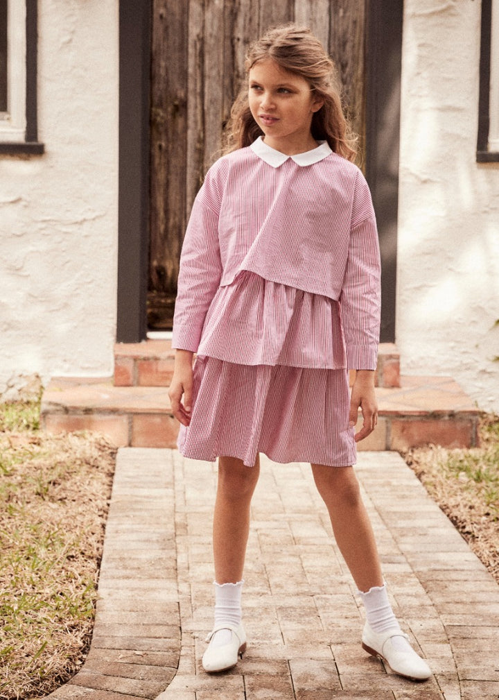 Young girl wearing a cropped long sleeve top with a peter pan collar and matching tier skirt standing outside on a walkway