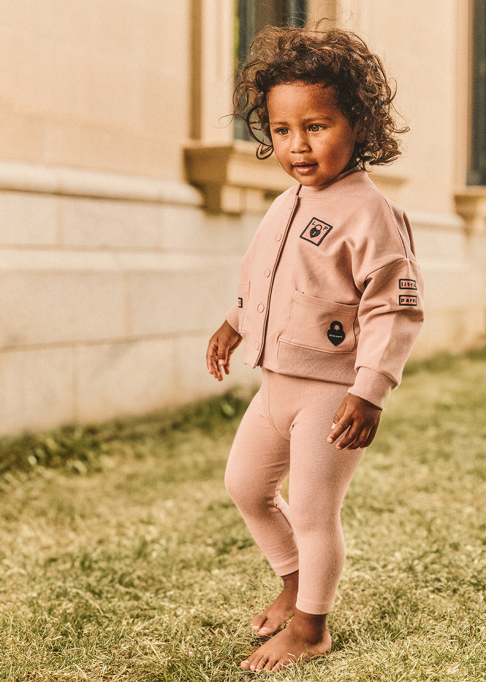 Baby wearing the Multi-Patch Baby Bomber Jacket in Pink.