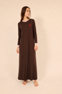 A woman modeling a long-sleeve brown maxi nightgown with a small red heart on the chest, standing against a solid beige studio background.