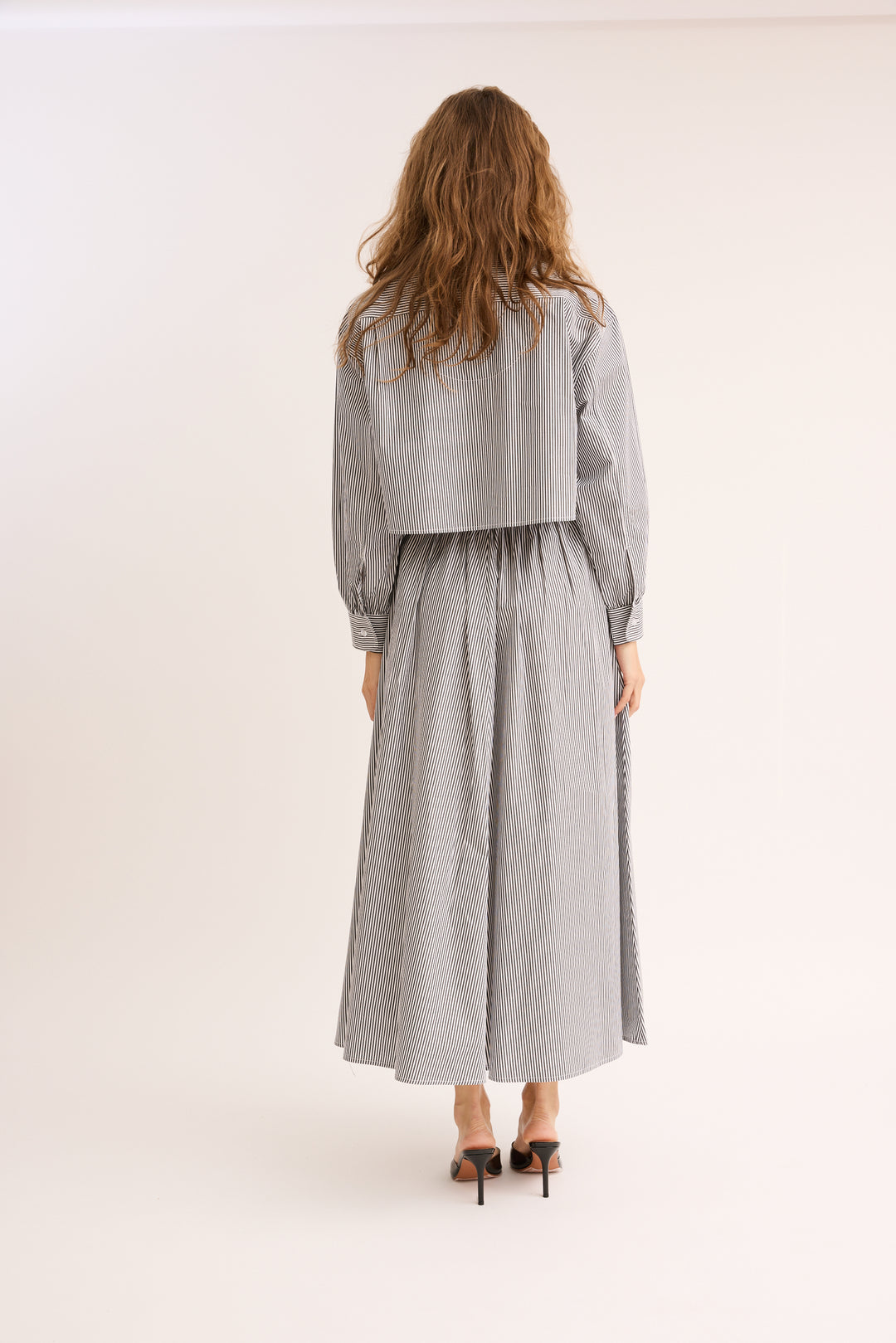 Model turned to show the back of the Striped Poplin Cropped Shirt and skirt.