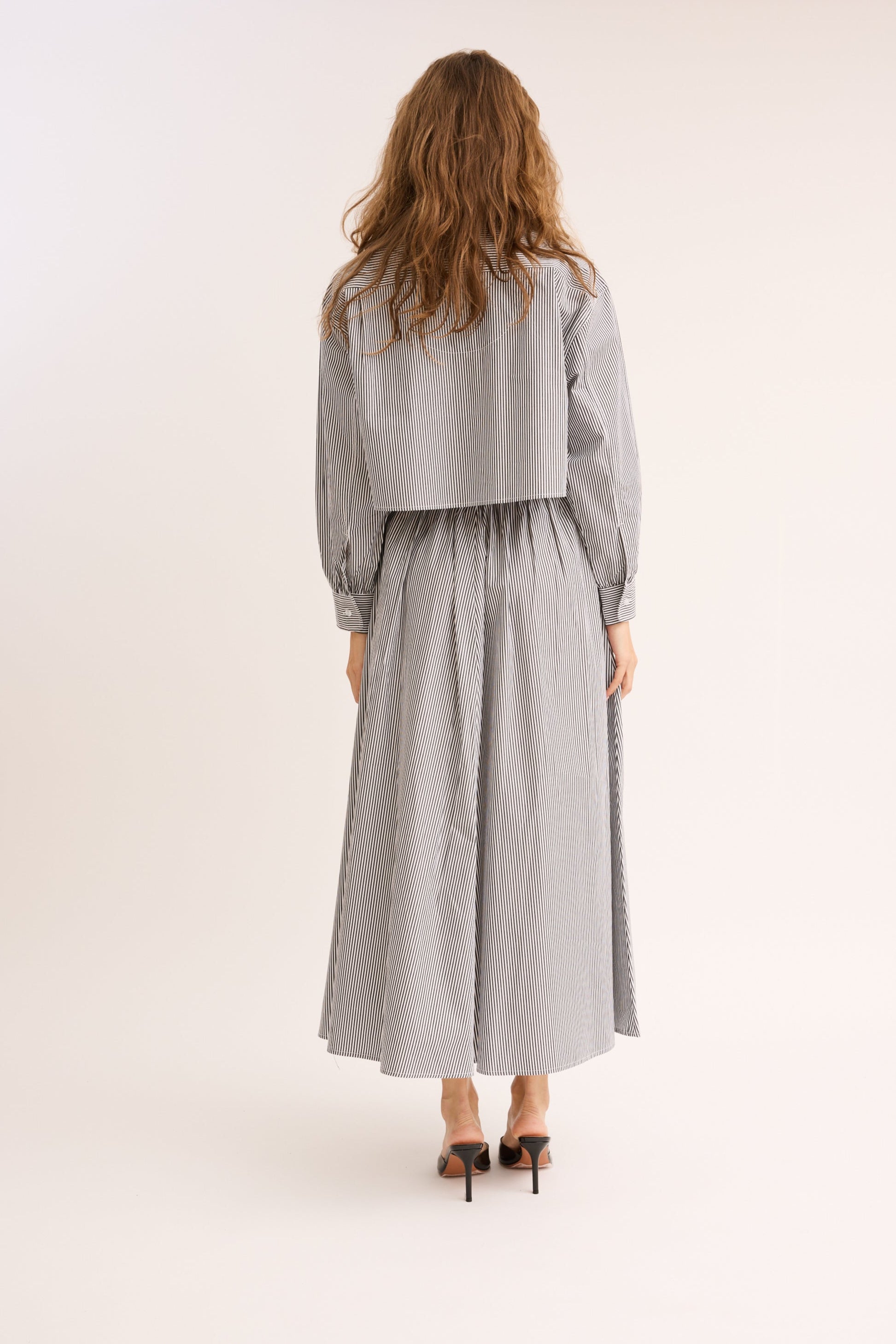 Model turned to show the back of the Striped Poplin Cropped Shirt and skirt.