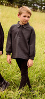 A young boy wearing a dark charcoal gray long-sleeve polo shirt and black pants standing in a grassy field.