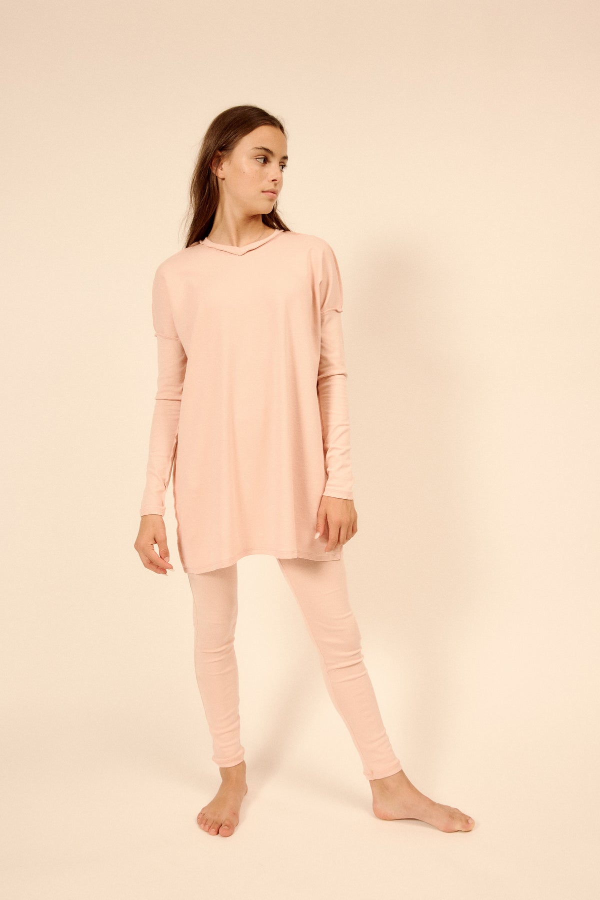 A young girl modeling a light pink long-sleeve top and matching pink Pajama leggings against a solid beige studio background.