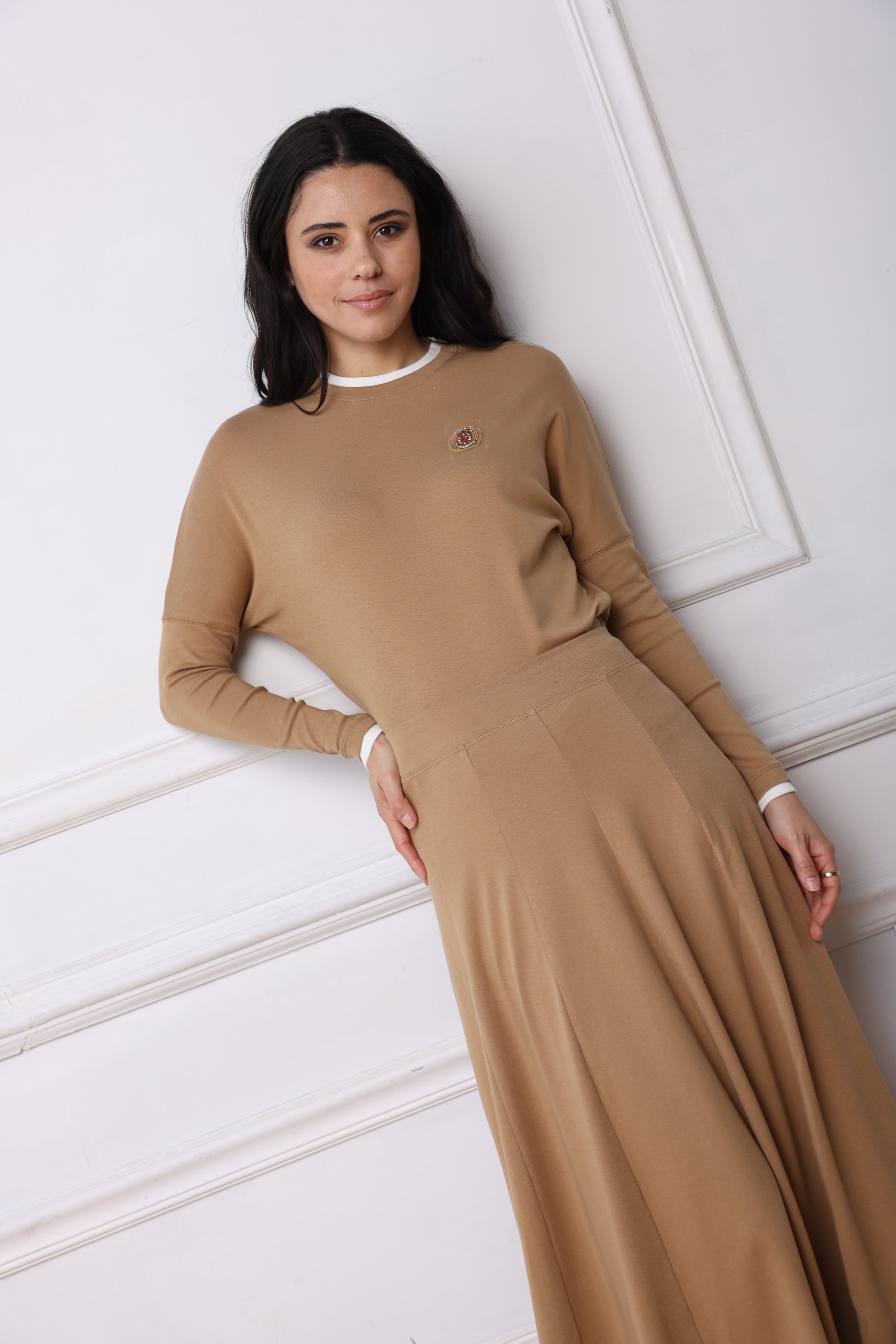 Woman wearing a long beige dress lying on a white floor.
