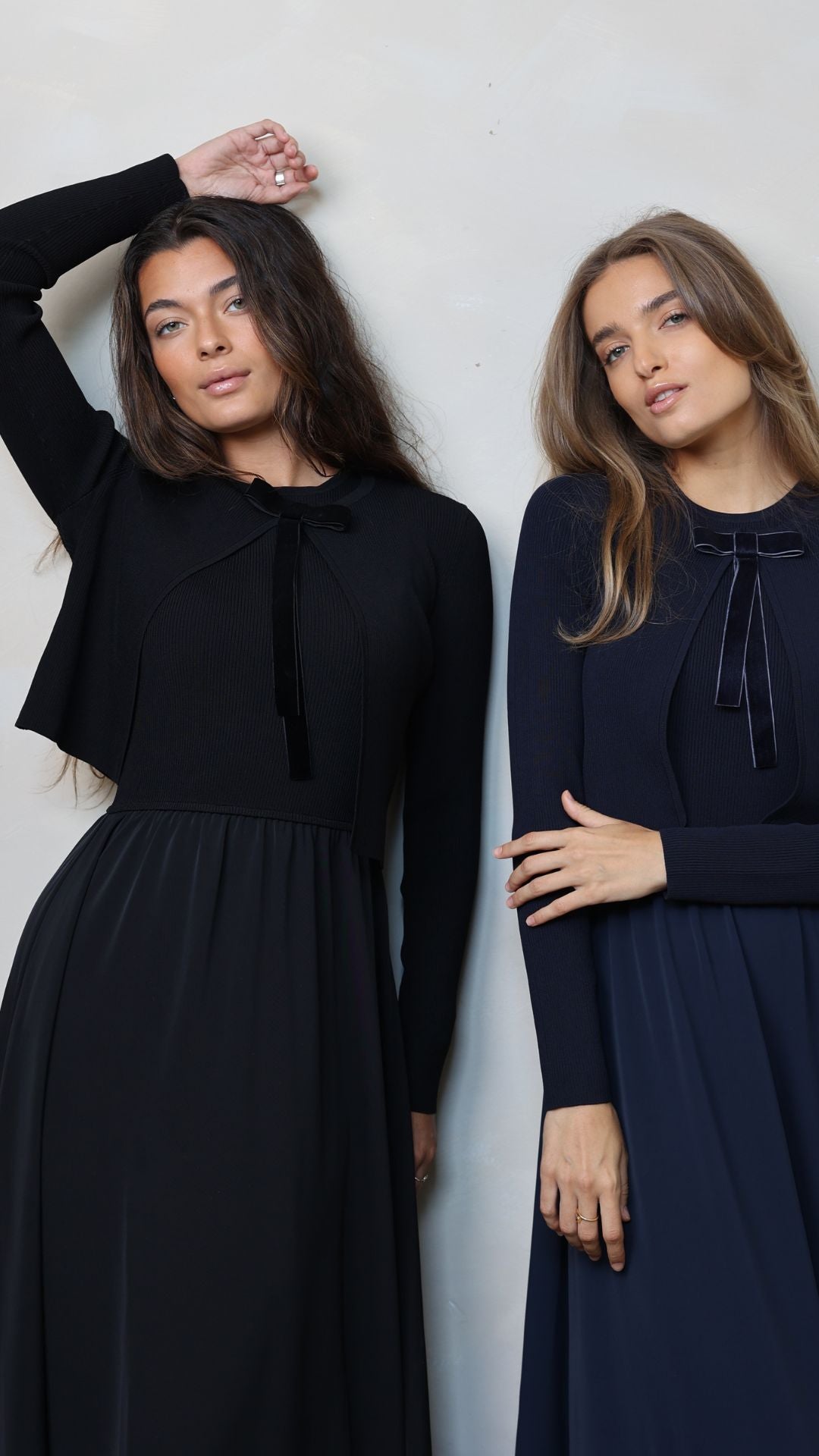 Two women wearing black and navy long dresses against a white background