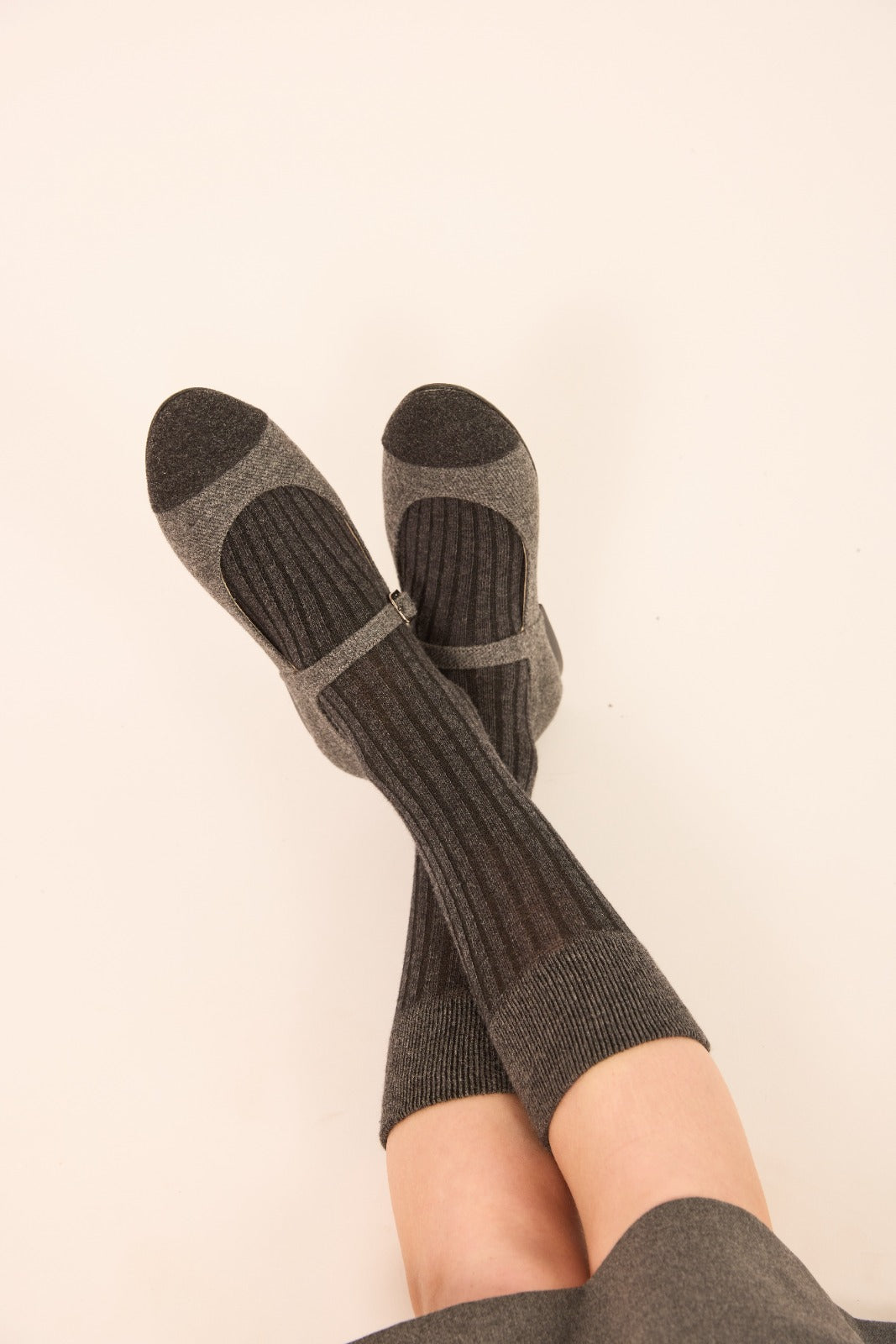 Dark gray ribbed crew socks with lighter gray toe and heel sections, worn on crossed legs against a plain off-white background.