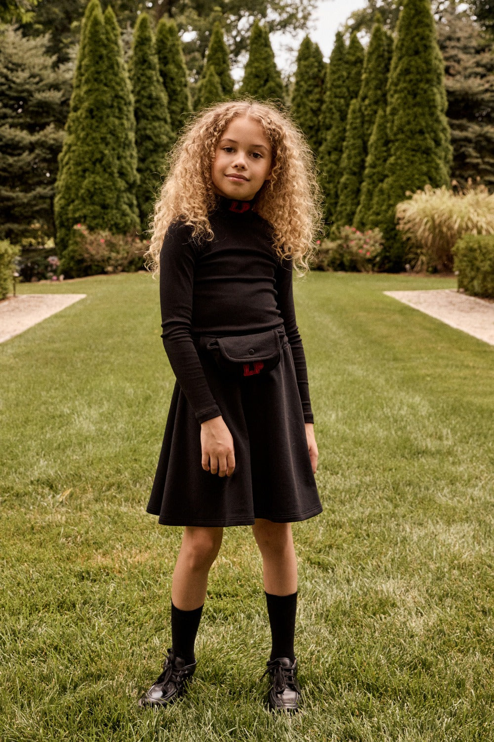Young girl in a black outfit standing on grass with trees in the background
