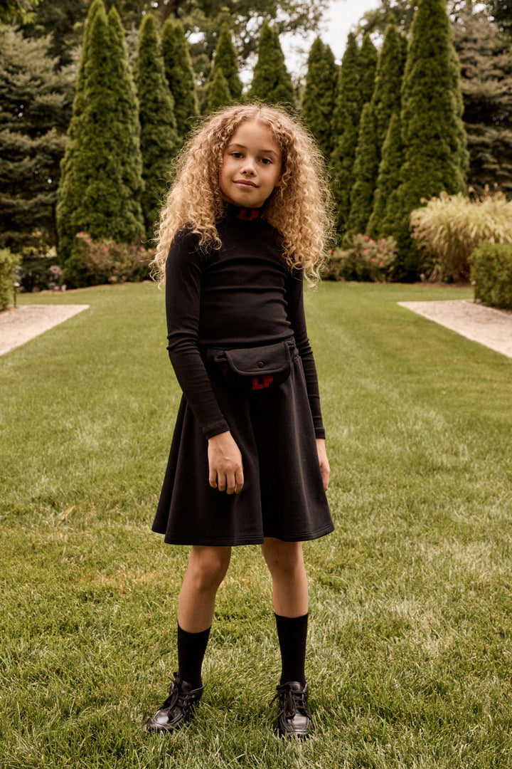 Young girl in a black outfit standing on grass with trees in the background