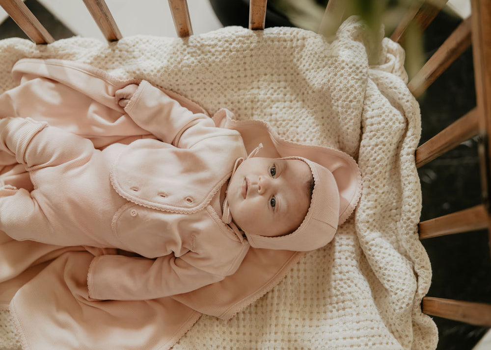 Baby in a pink outfit lying on a textured blanket