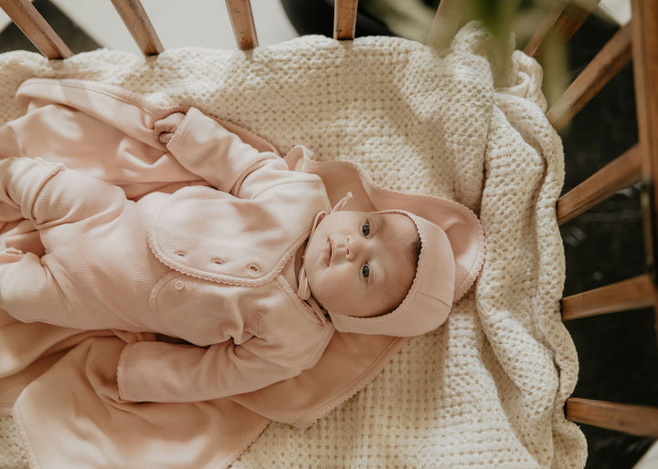Baby in a pink outfit lying on a textured blanket